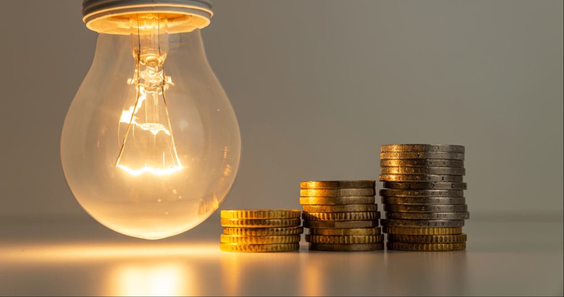 Illuminated light bulb beside stacked coins