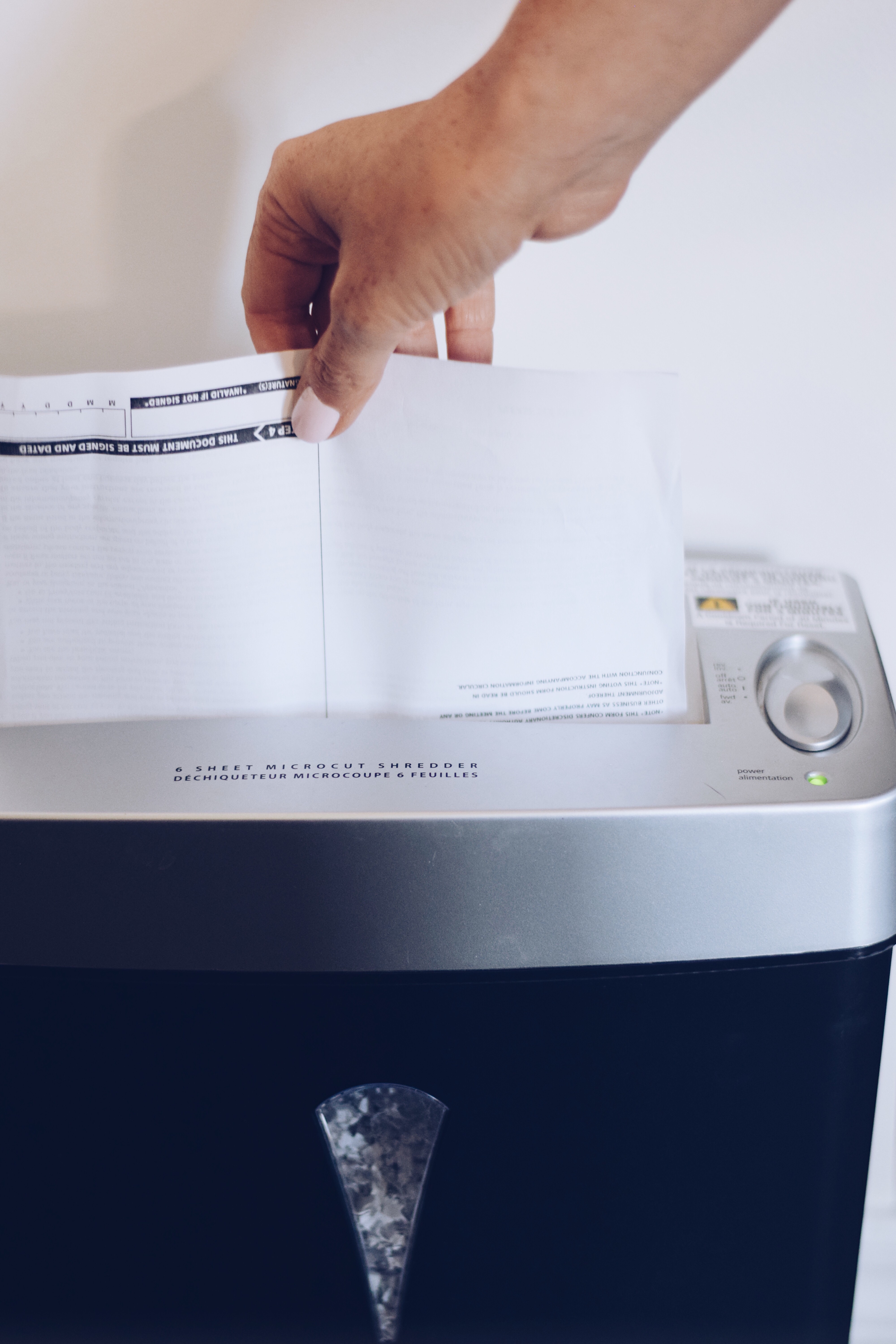 A hand feeds a white paper document into the slot of a black and silver micro-cut paper shredder
