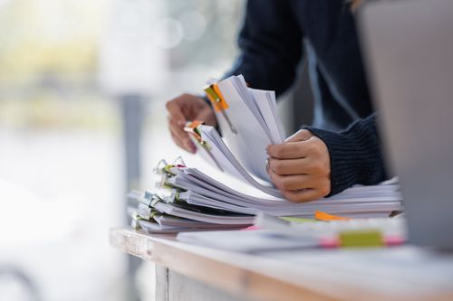 Close-up of a person's hands sorting a large, stacked pile of paper documents secured with binder clips on a desk