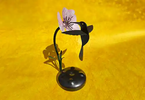 Recycled Metal Humming Bird Sculpture featuring a green stemmed pink and leaves with a black iridescent humming bird feeding from the pink flower