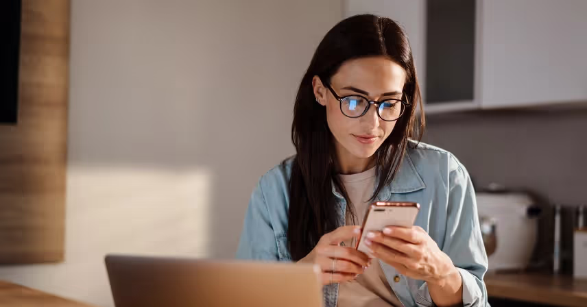 woman in kitchen looking at cell phone and laptop