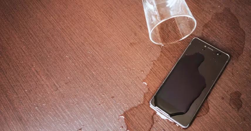 a cell phone and spilled glass of water on a table