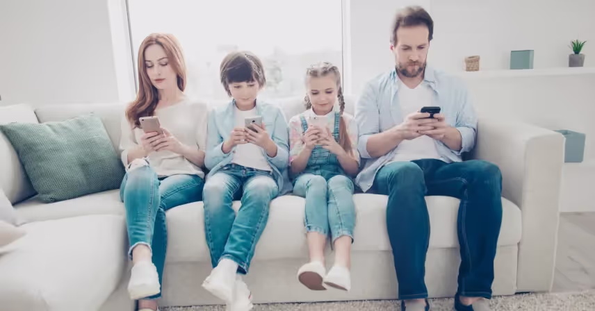 a family of four sitting on a couch and using their cell phones