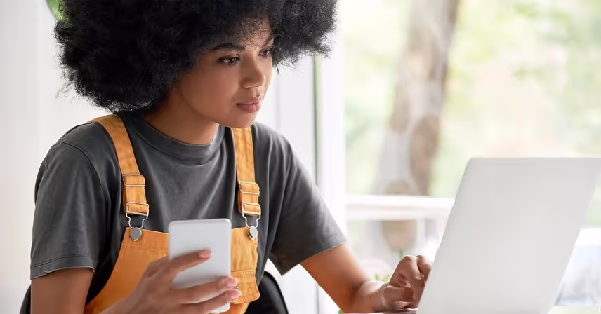 a person looking at a laptop and holding a cell phone