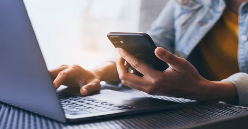 a person holding a phone and typing on a laptop