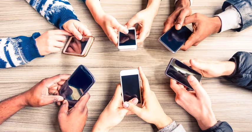 overhead view of a circle of hands using phones on a table
