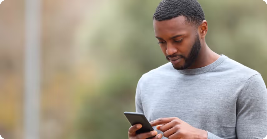 a man is standing outdoors holding a smartphone in his hand