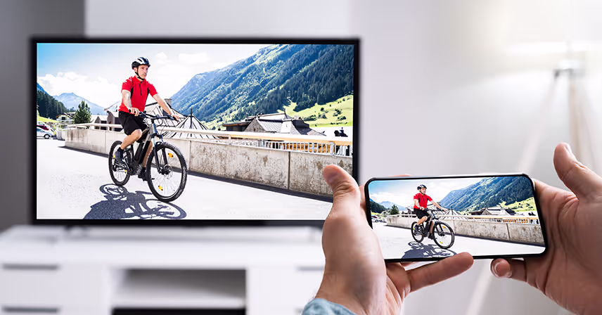 Man holds an Apple iPhone with an image of a bicycle rider that is duplicated on television on front of him.