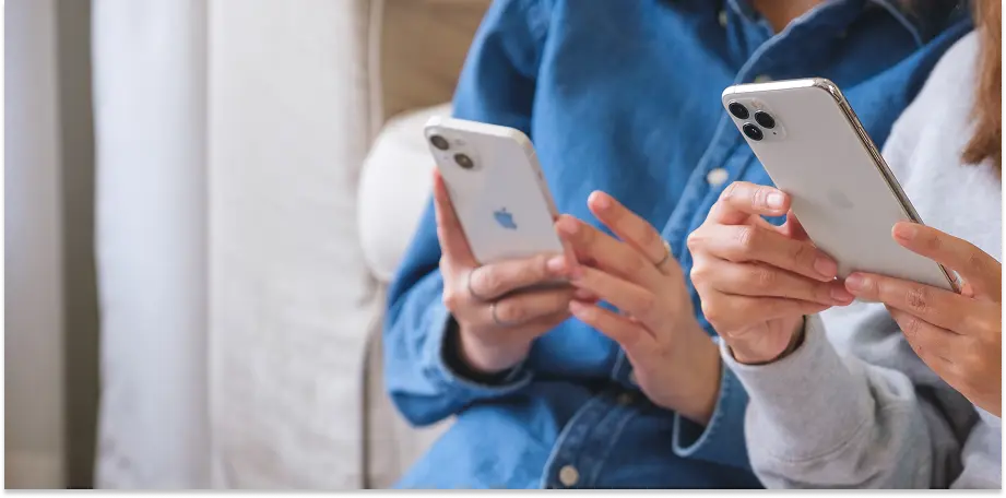 two people sitting at a table looking at mobile phones