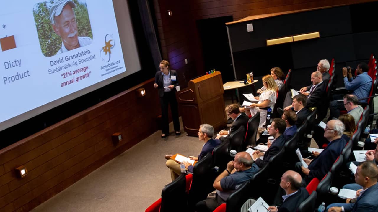 A founder presents data slides to a packed auditorium of investors and attendees at a Wisconsin startup pitch competition