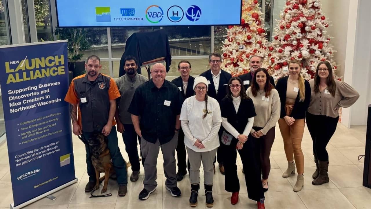 Finalists and organizers pose together at the NEW Launch Alliance regional pitch event at TitletownTech in Green Bay, with sponsor logos on the screen behind them.
