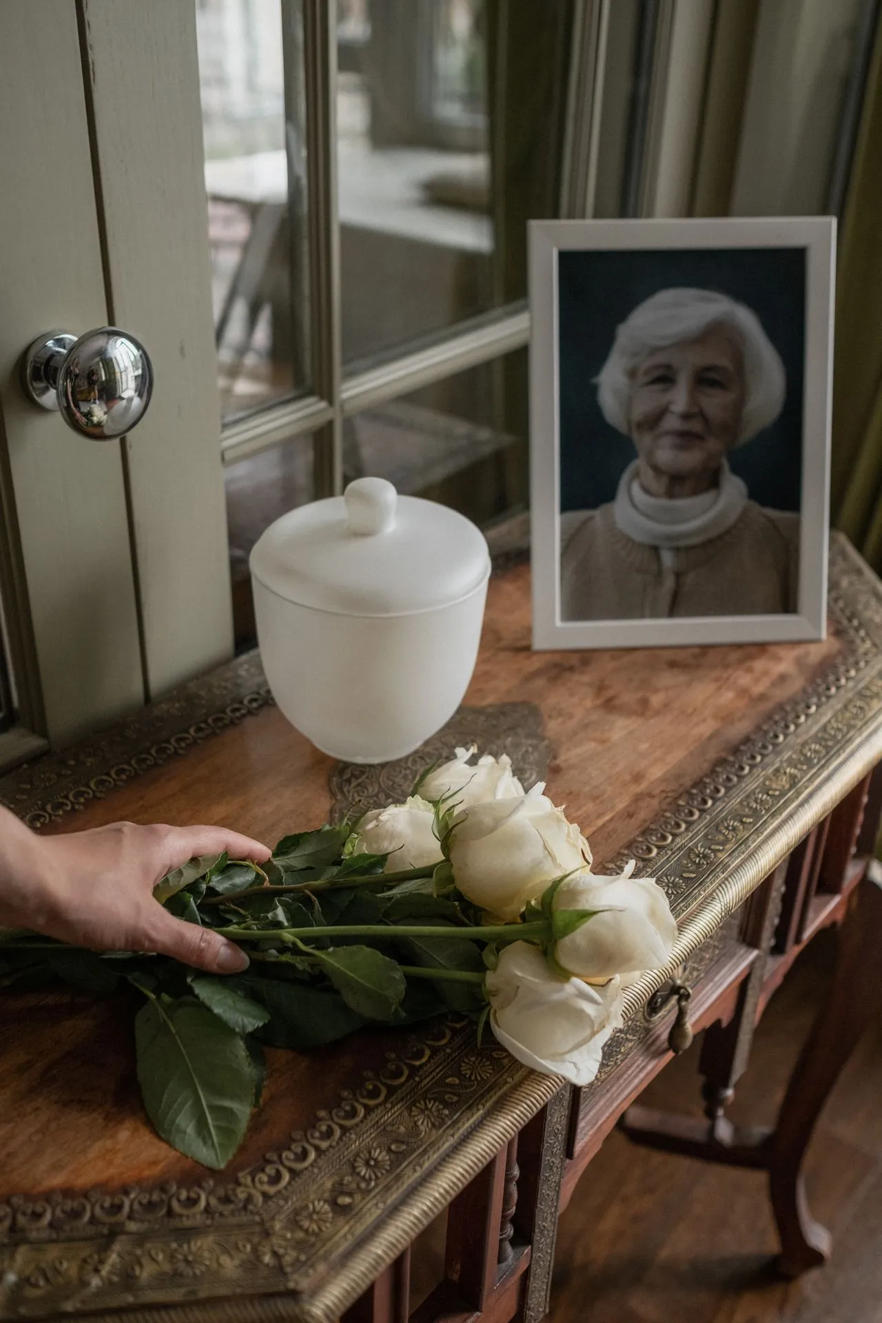 An urn and white roses on a hallway table beside a framed photograph