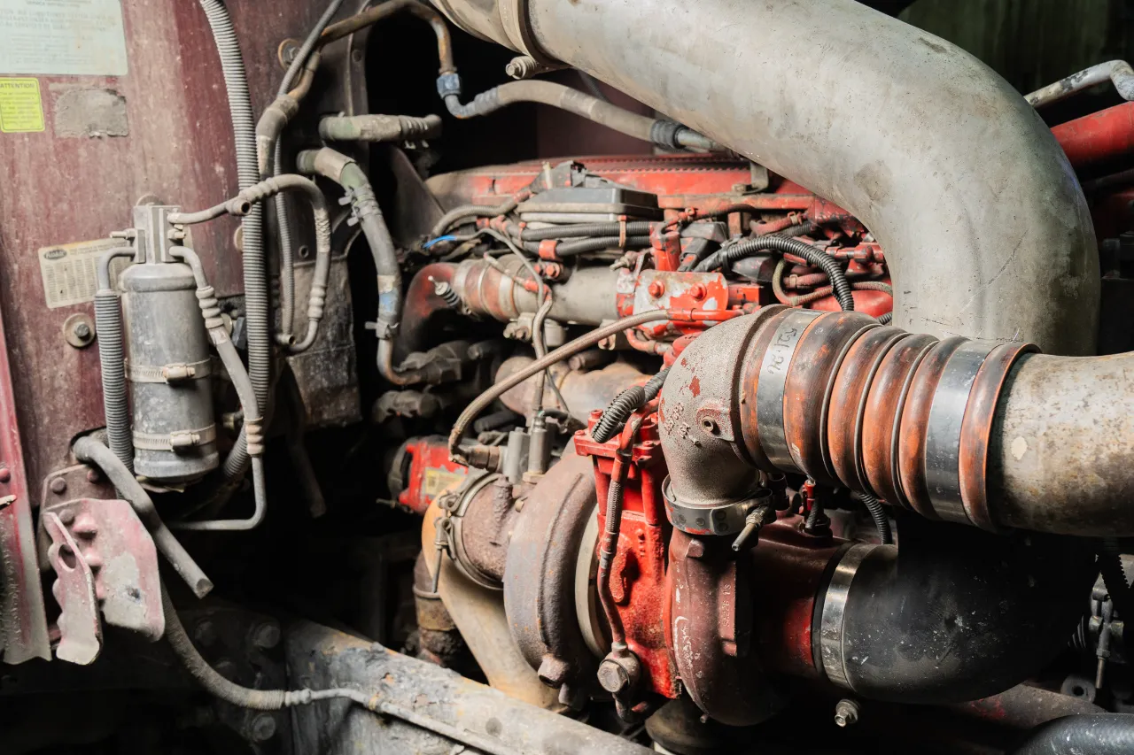 Diesel engine with red components and large turbocharger piping inside a heavy-duty truck.