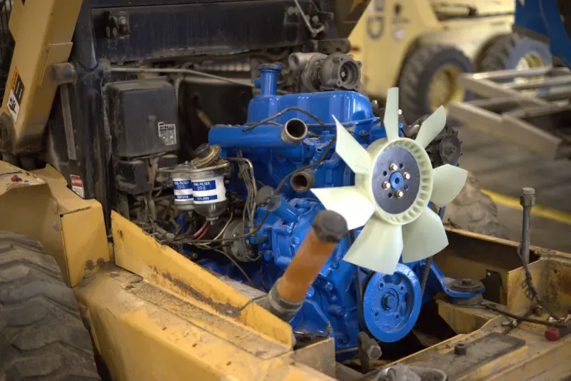 Coolant repair on a heavy-duty engine installed in construction equipment with cooling fan and components exposed.