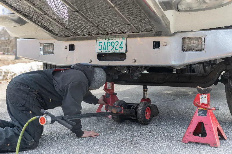 Roadside shoulder repairs on a heavy-duty truck with a technician using jacks beneath the front axle.