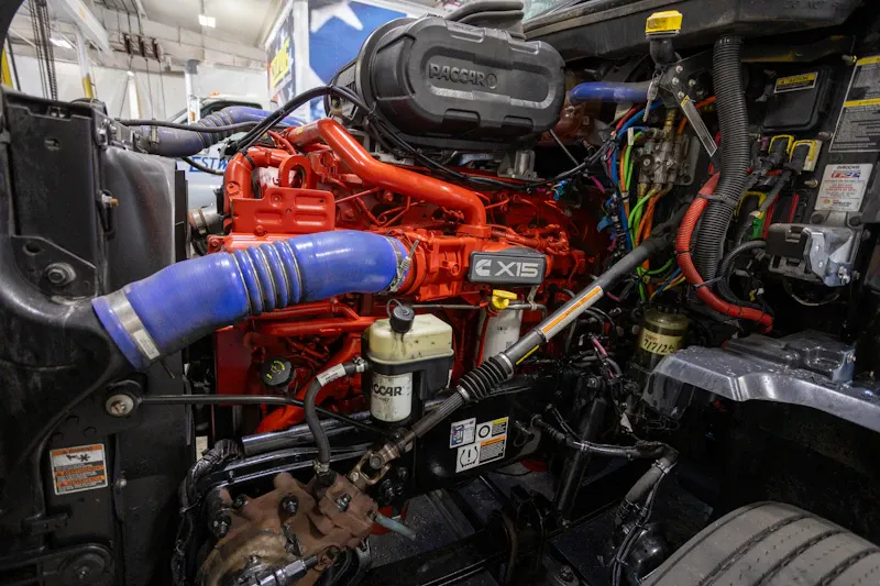 Heavy-duty repair on a Cummins X15 engine with the hood open for service. PACCAR branding is visible on the engine cover.