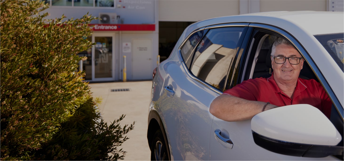 Smiling driver in red shirt sitting in white car near building entrance