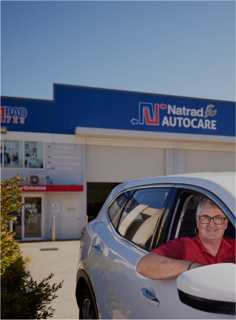 Smiling man in red shirt sits in car outside Natrad Autocare service center