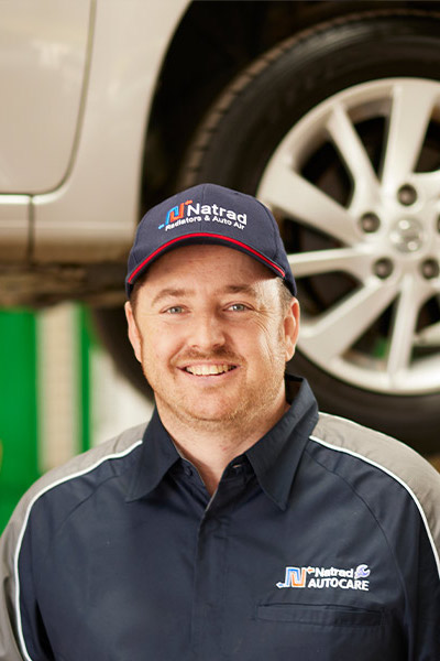 Smiling auto care technician in uniform standing next to car wheel