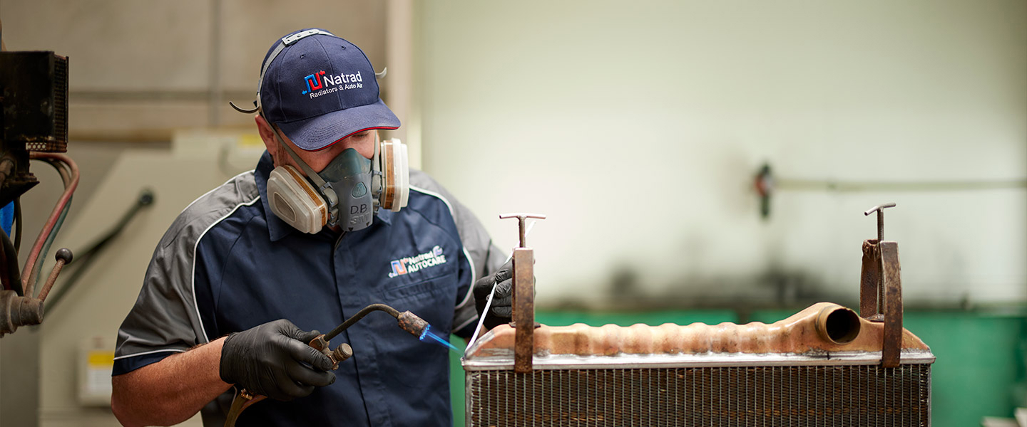 Technician in safety gear welding a radiator in industrial workshop