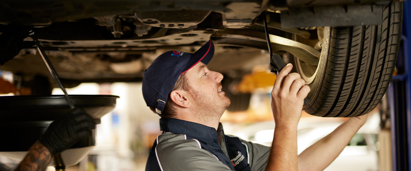 Mechanic inspecting car tire and undercarriage in auto repair shop