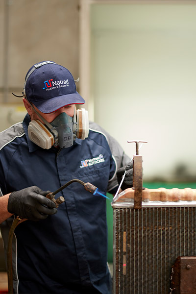 Technician welding with protective gear and torch near industrial equipment