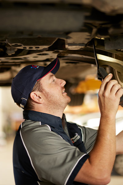 Mechanic inspecting underside of vehicle with flashlight in auto repair shop