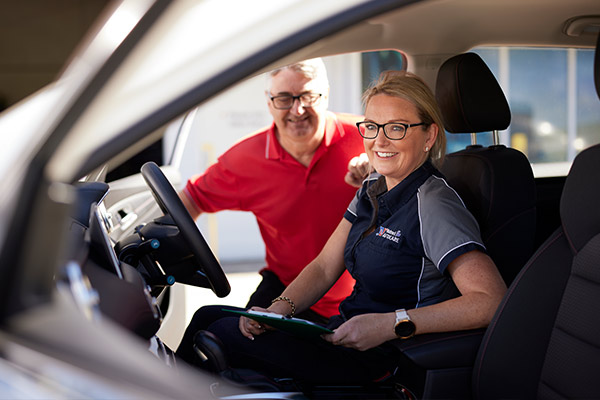 Smiling coworkers in car, one in red shirt, one in blue uniform