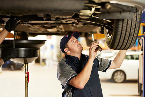 Mechanic inspecting underneath a car on a lift in auto repair shop