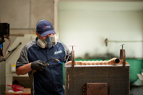 Worker in protective gear inspects industrial radiator in workshop