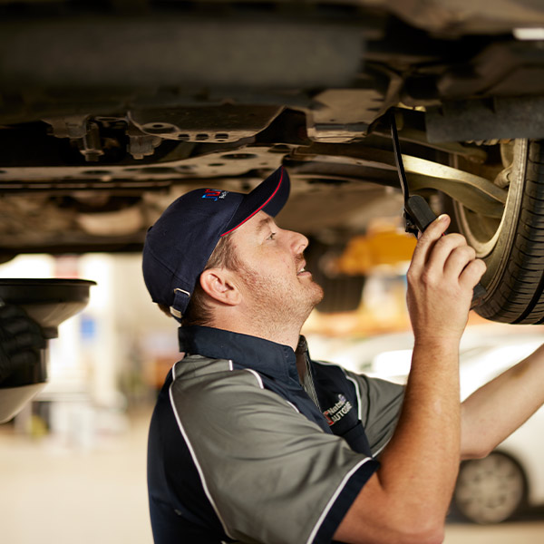 Mechanic inspecting car undercarriage with flashlight in auto repair shop