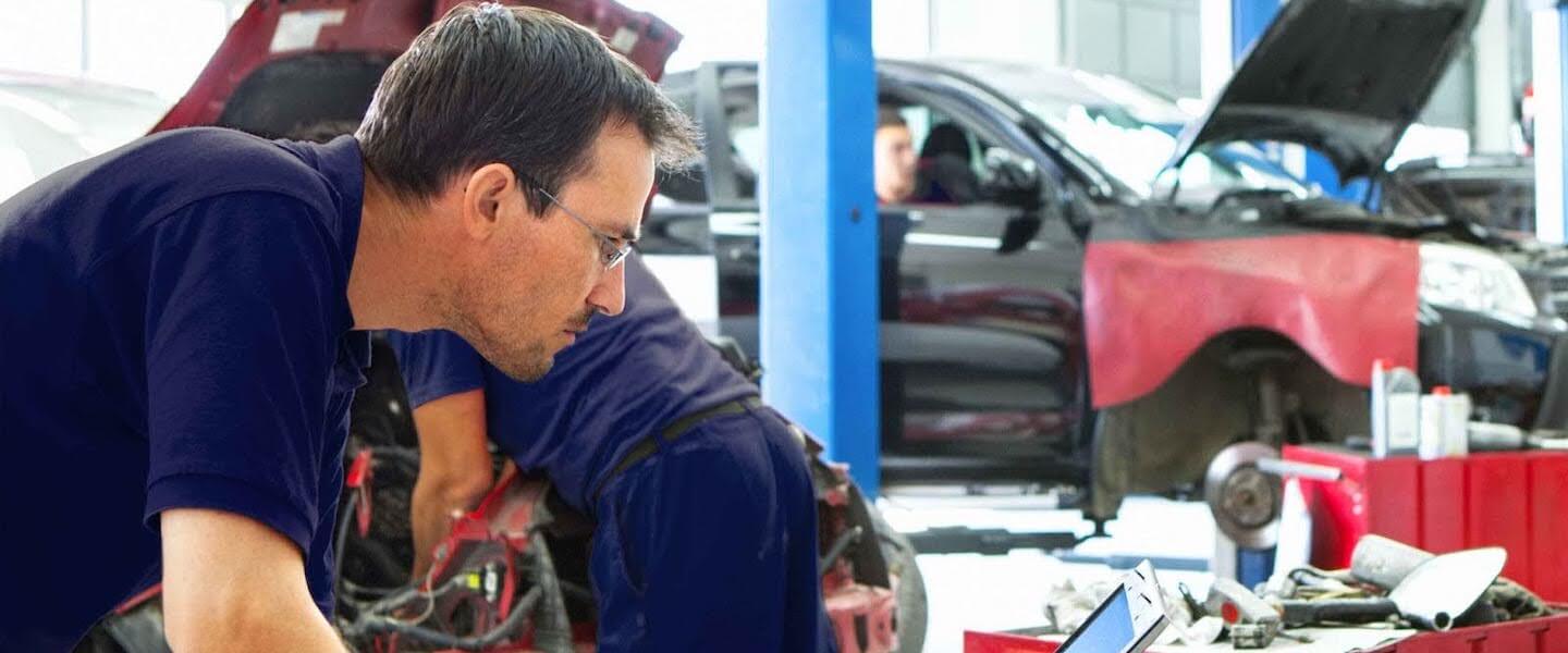Mechanic in blue shirt working on car engine in auto repair shop