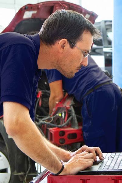 Mechanic in blue shirt working on laptop near open car hood