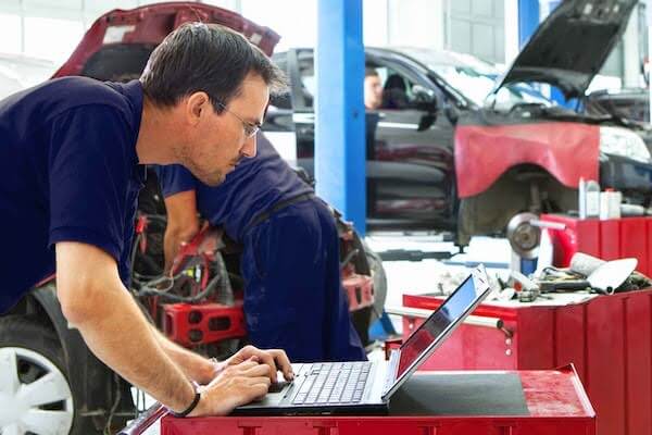 Mechanic using laptop while working on car in auto repair shop