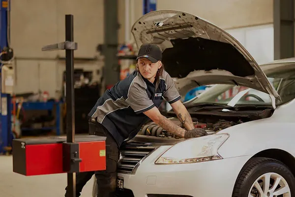 Mechanic in cap checking car engine in automotive repair shop