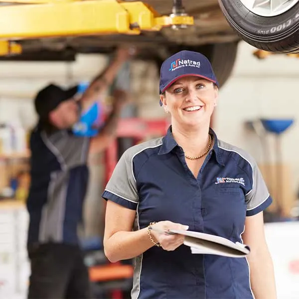 Smiling worker in navy uniform and cap standing in automotive workshop