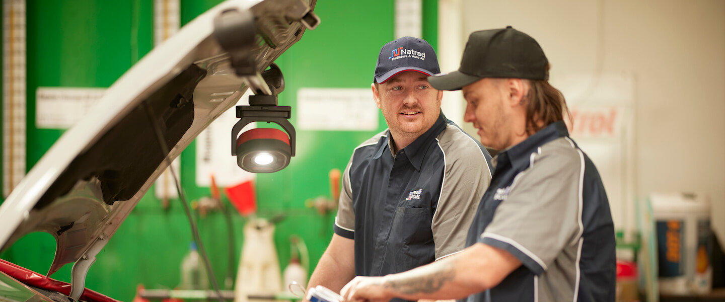 Automotive technicians in Natrad uniform working on a vehicle repair