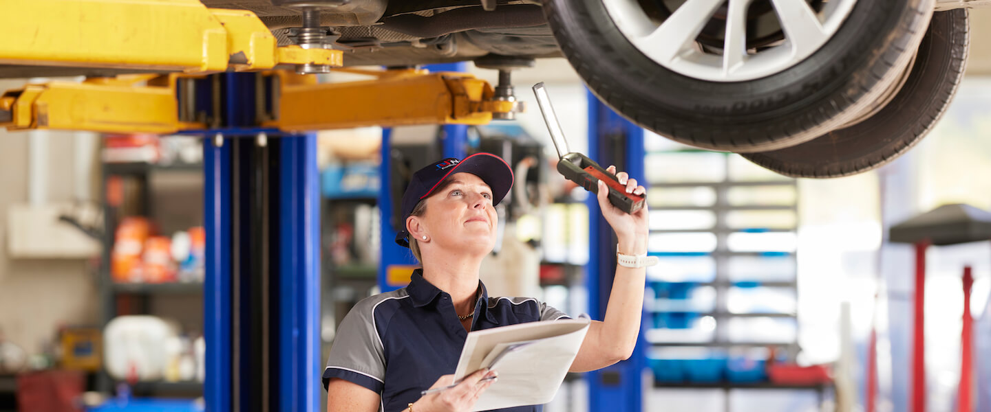 Mechanic inspecting car underneath vehicle lift with diagnostic tool