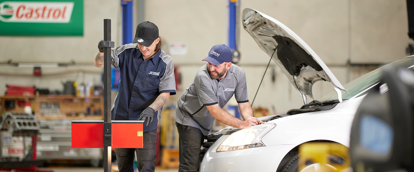 Automotive technicians working on a white car in a service garage