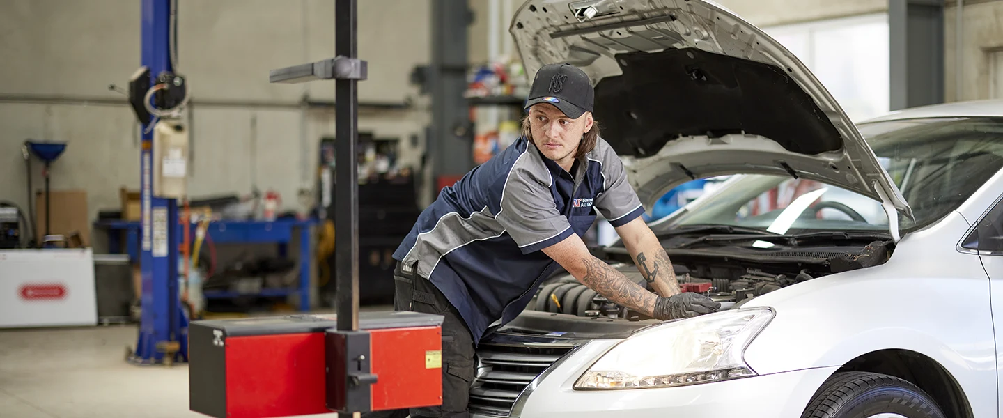 Mechanic in uniform checking under hood of white car in auto repair shop