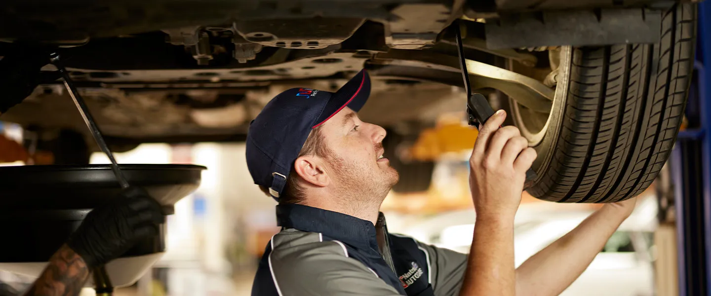 Mechanic inspecting car tire and undercarriage in automotive repair shop