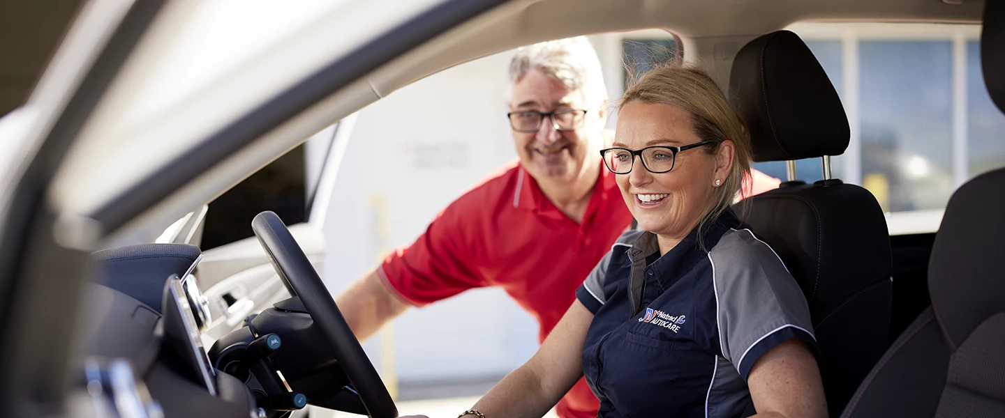 Smiling automotive staff member in car with colleague at dealership