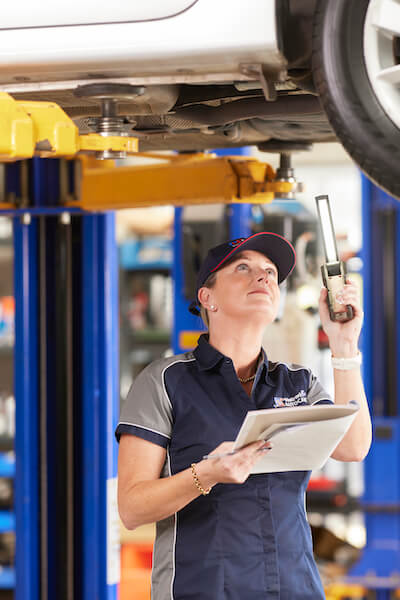 Mechanic inspecting vehicle undercarriage with clipboard and flashlight