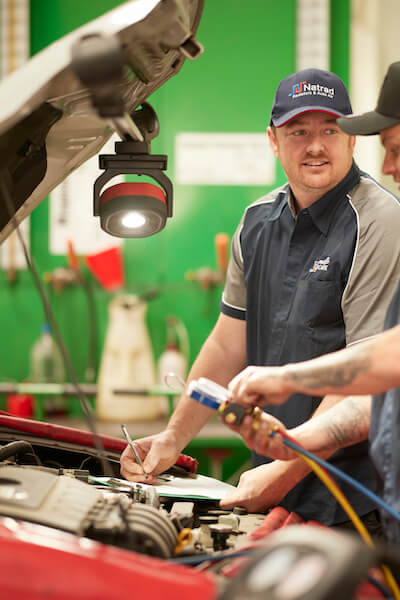Auto mechanic working on car engine under workshop light