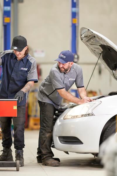 Mechanics examining a white car in an auto repair shop with lift