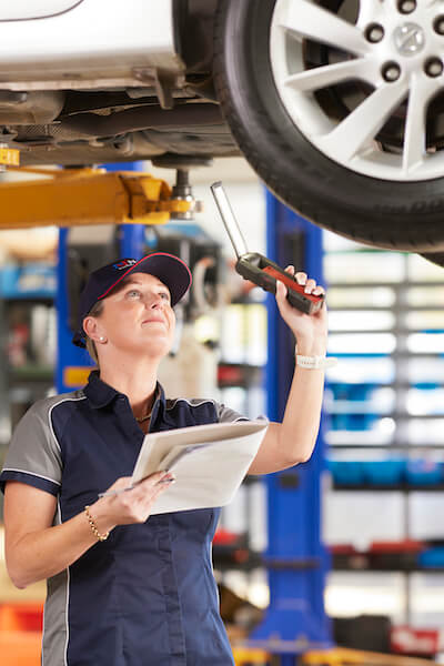 Automotive technician inspecting car undercarriage with wrench and clipboard