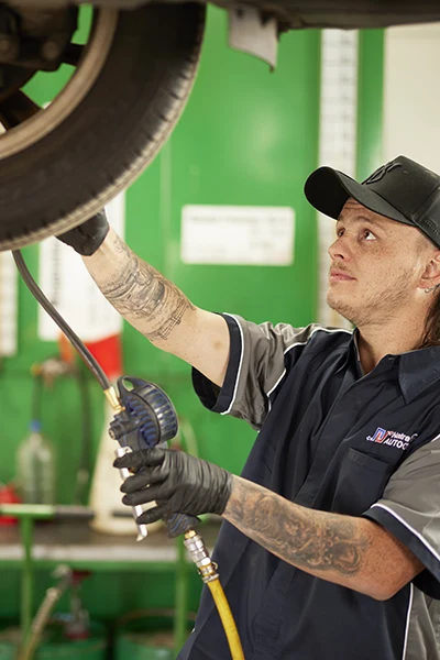 Mechanic with tattoos checking tire pressure in automotive service center
