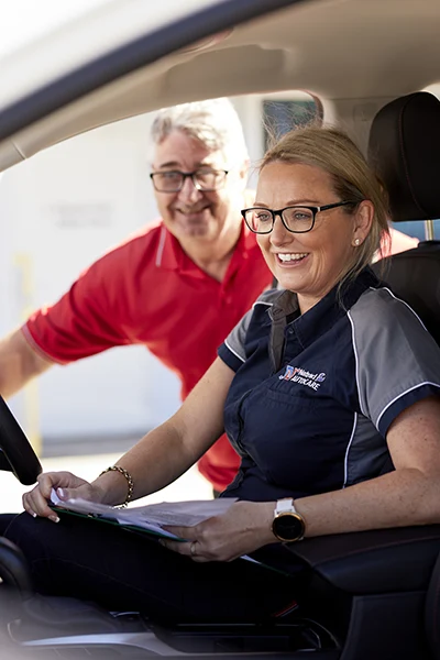 Two smiling colleagues in car, discussing work and wearing glasses