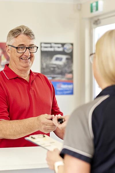 Smiling employee in red shirt assists customer at service counter