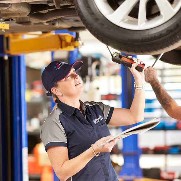 Mechanic working on car undercarriage with tool and clipboard